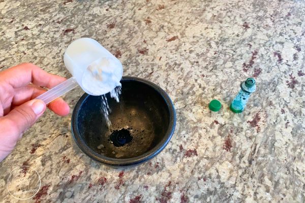 Someone prepping for the Harry Potter SEL Sorting Hat activity. There is baking soda being dropped in a small black bowl with a a few drops of green food coloring both in the bowl and the bottle sitting near by