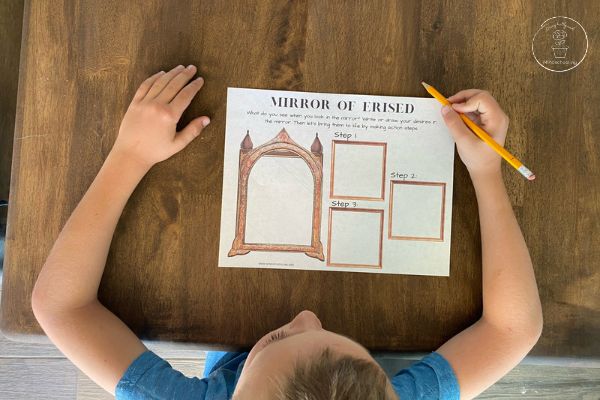 Harry Potter Mirror of Erised Activity - An overhead picture of a child sitting at the table, holding a pencil, preparing to complete the printable worksheet