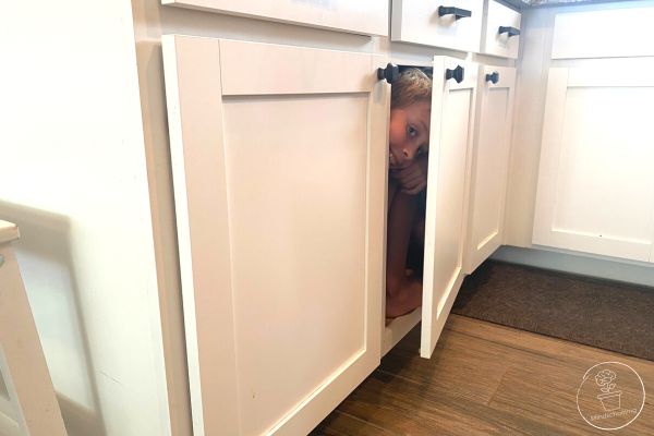 A child hiding in a cupboard, peeking out of the cracked open door